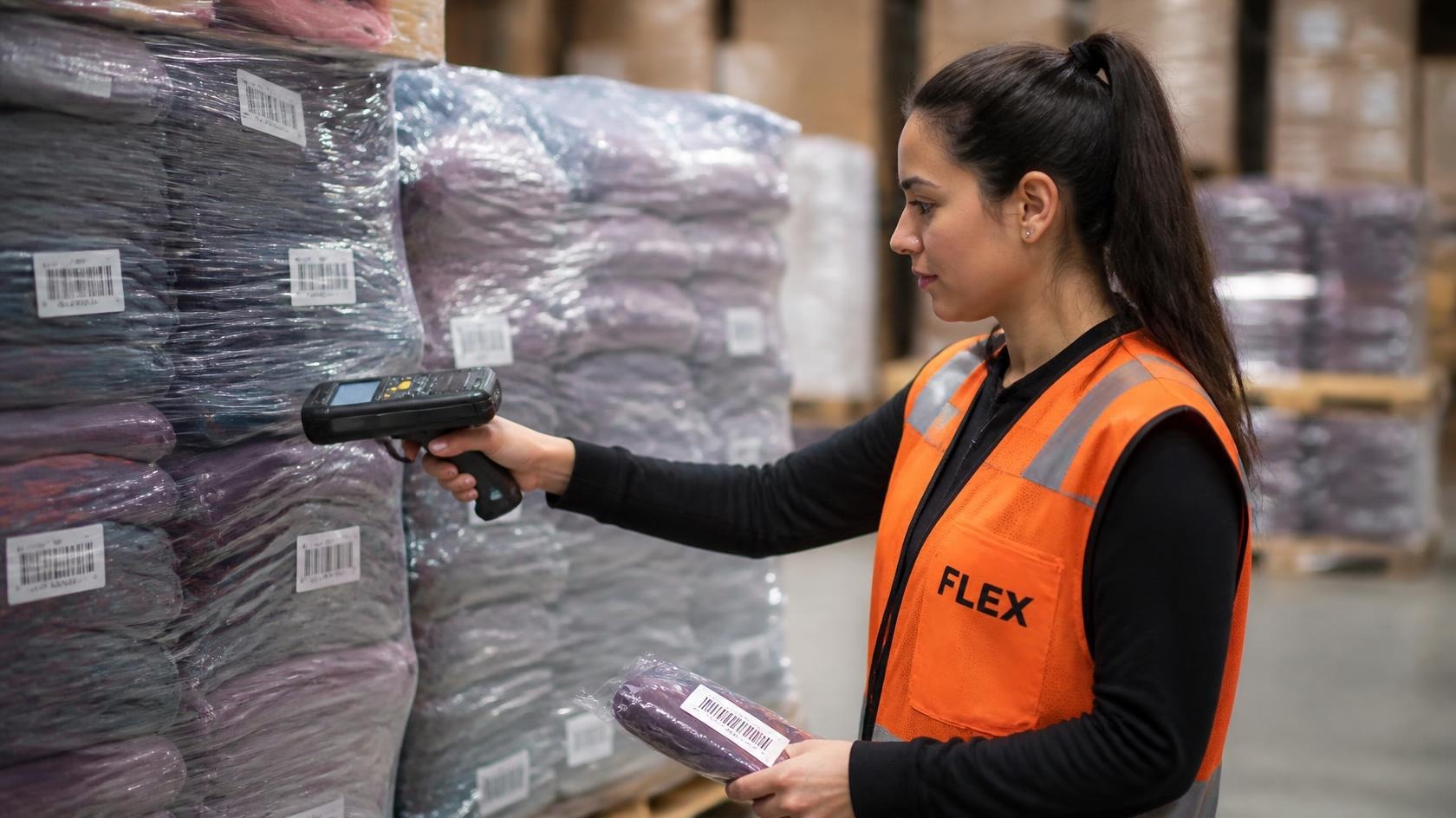 Quality control auditor wearing an industrial orange safety vest scanning FNSKU barcode stickers on wrapped activewear with an RF reader.